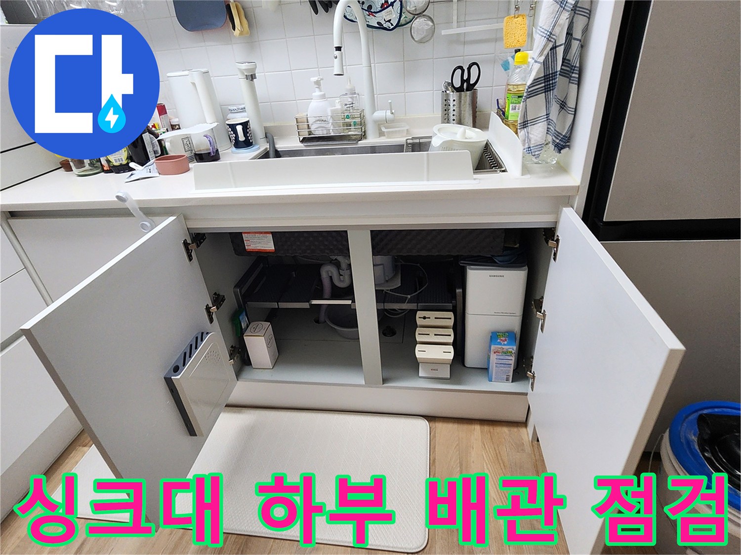 열려 있는 싱크대 아래 하부장 내부의 배관 및 분배기 구조