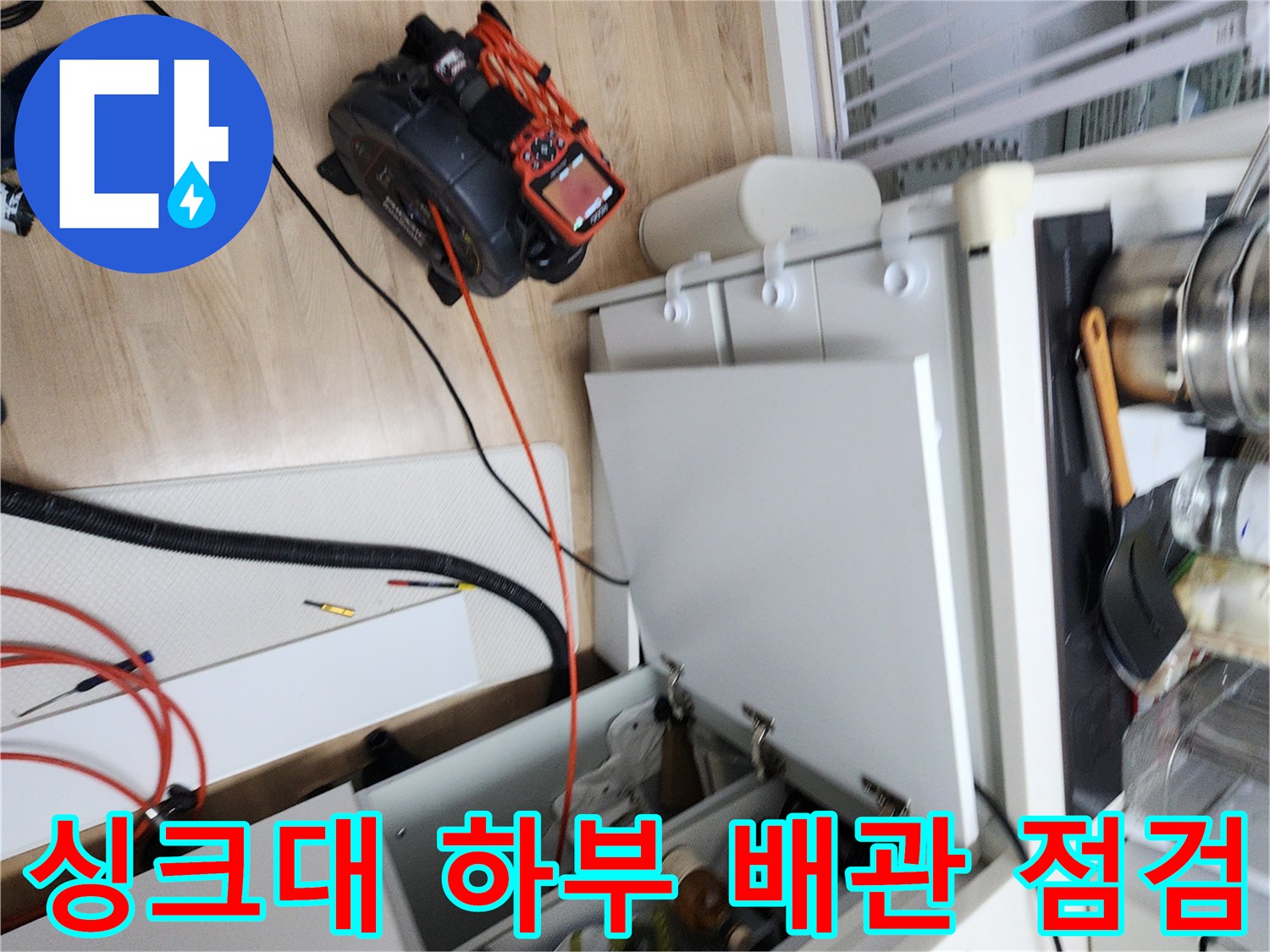 하부장 아래쪽 바닥 배관과 주변 장비를 배치한 현장 사진입니다.