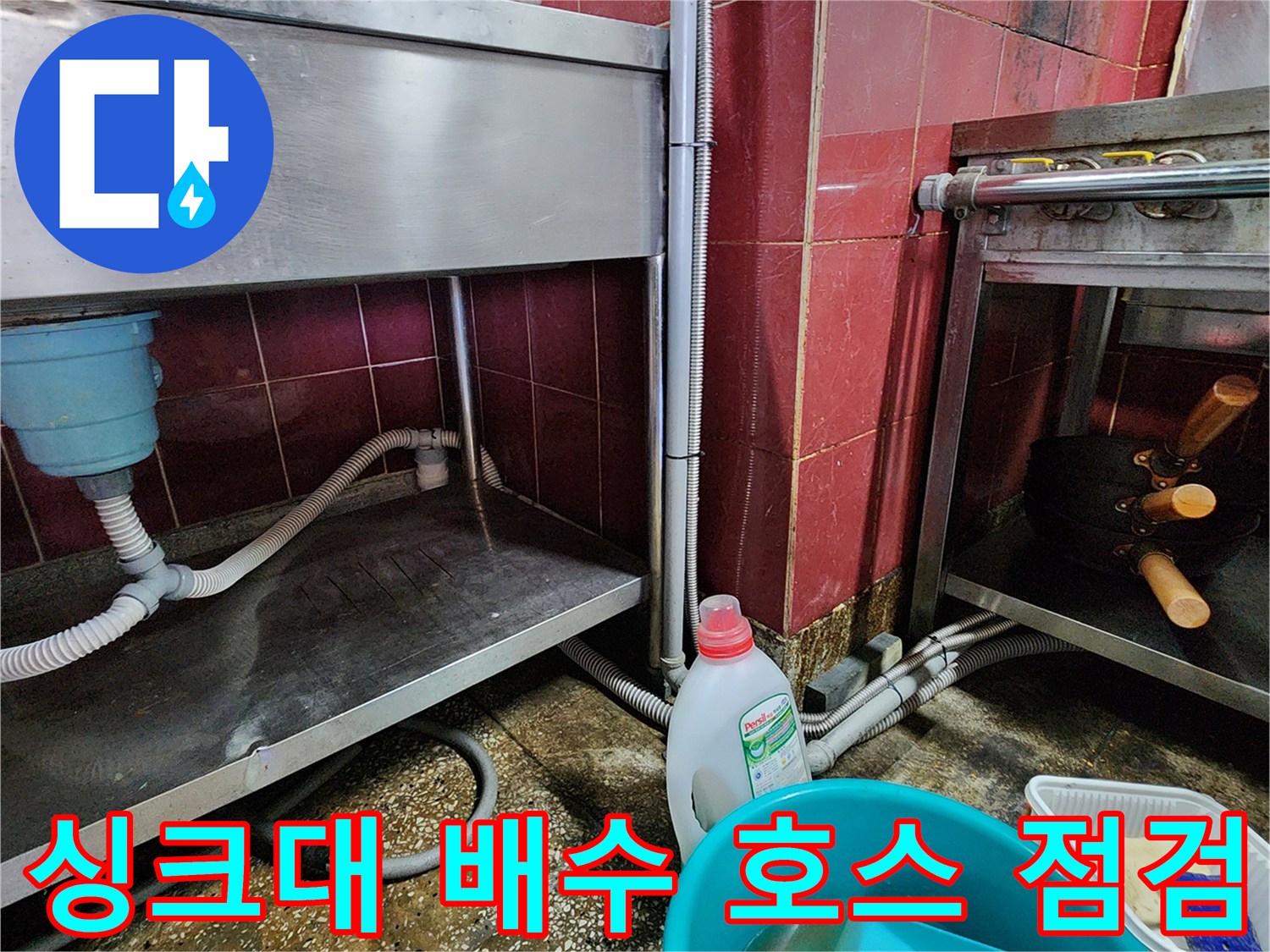 스테인리스 싱크대 하단에 연결된 굵은 배수 호스와 주변 환경