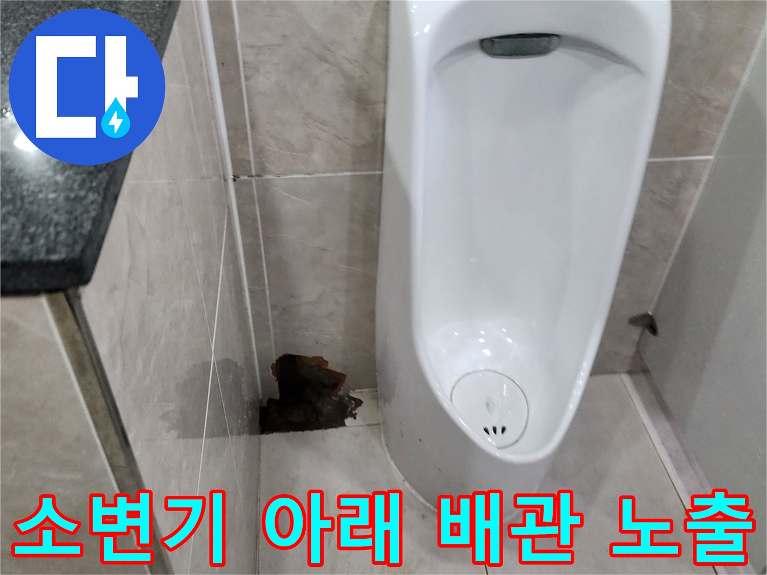 소변기 옆 타일이 깨져 내부 배관의 파손 부위가 드러난 사진입니다.