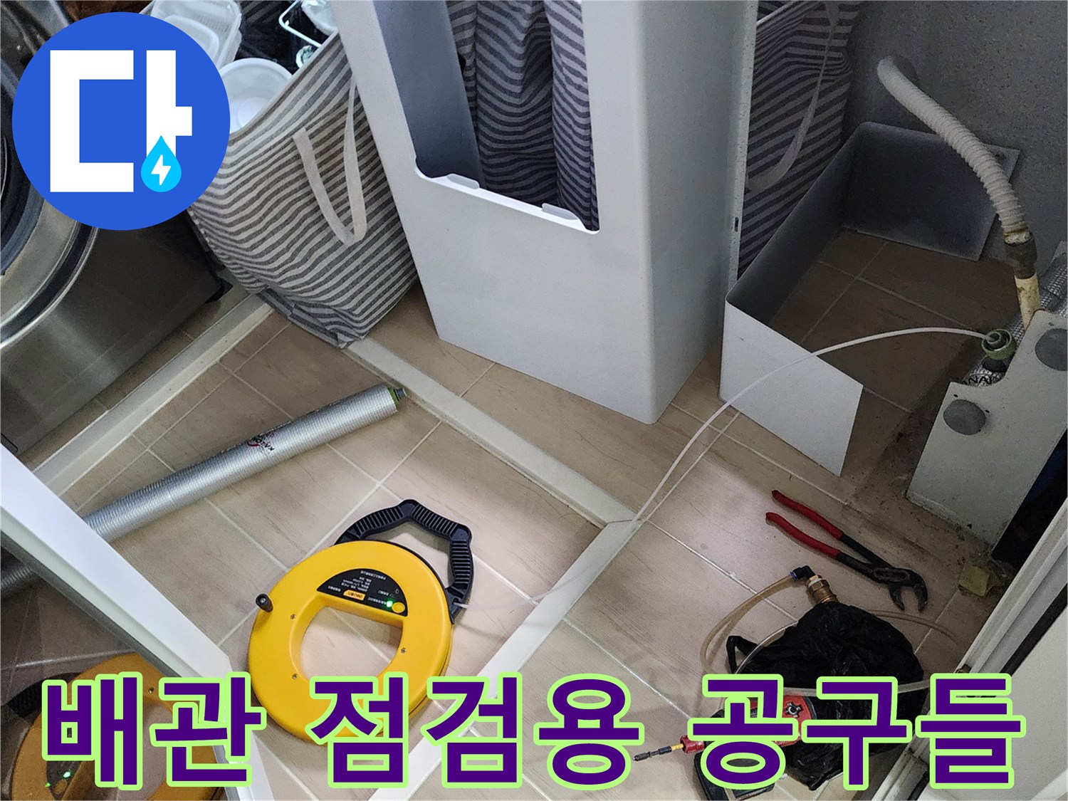 세탁기 아래 공간에서 진행 중인 배관 압력 테스트와 드릴 작업 도구의 모습
