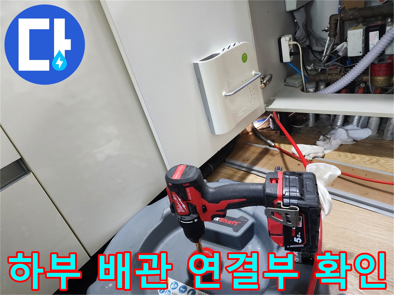 전동 공구를 사용하여 싱크대 하부의 배관 결함을 점검하는 장면입니다.
