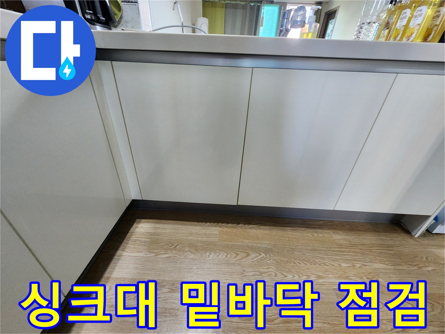주방 싱크대 아래쪽 바닥재와 가구 마감 부위를 촬영한 사진입니다.