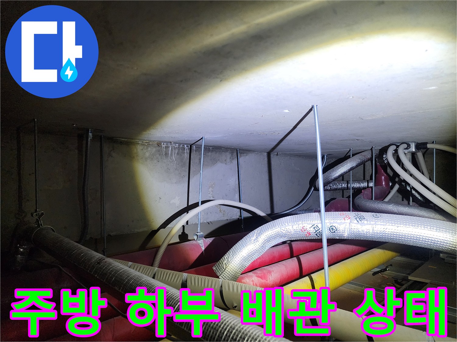 주방 싱크대 하부의 은박 보온재로 감싸진 복잡한 배관 구조 모습