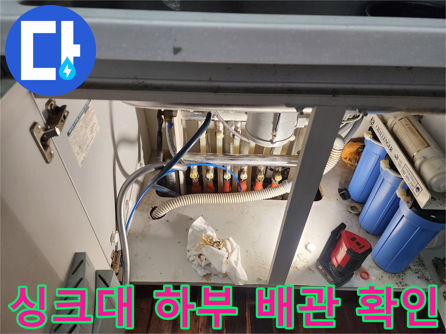 싱크대 하부장 내부의 정수 필터와 급수 호스 연결 부위 상세 사진