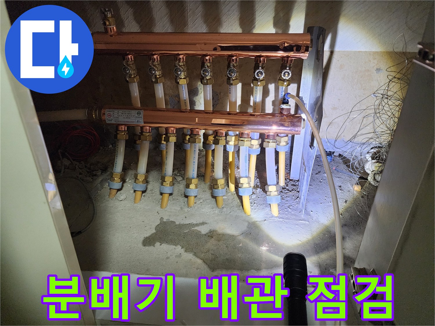 싱크대 하부장 내부에 노출된 난방 분배기와 연결 배관 상태