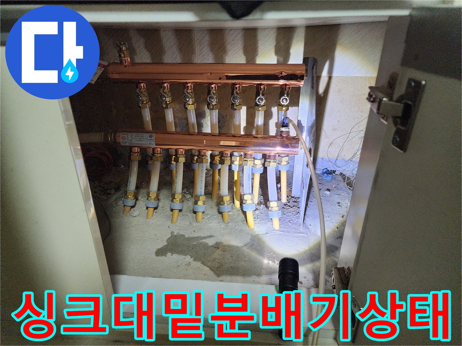 싱크대 하부장 내부의 난방 분배기와 연결된 배관 구조물 사진