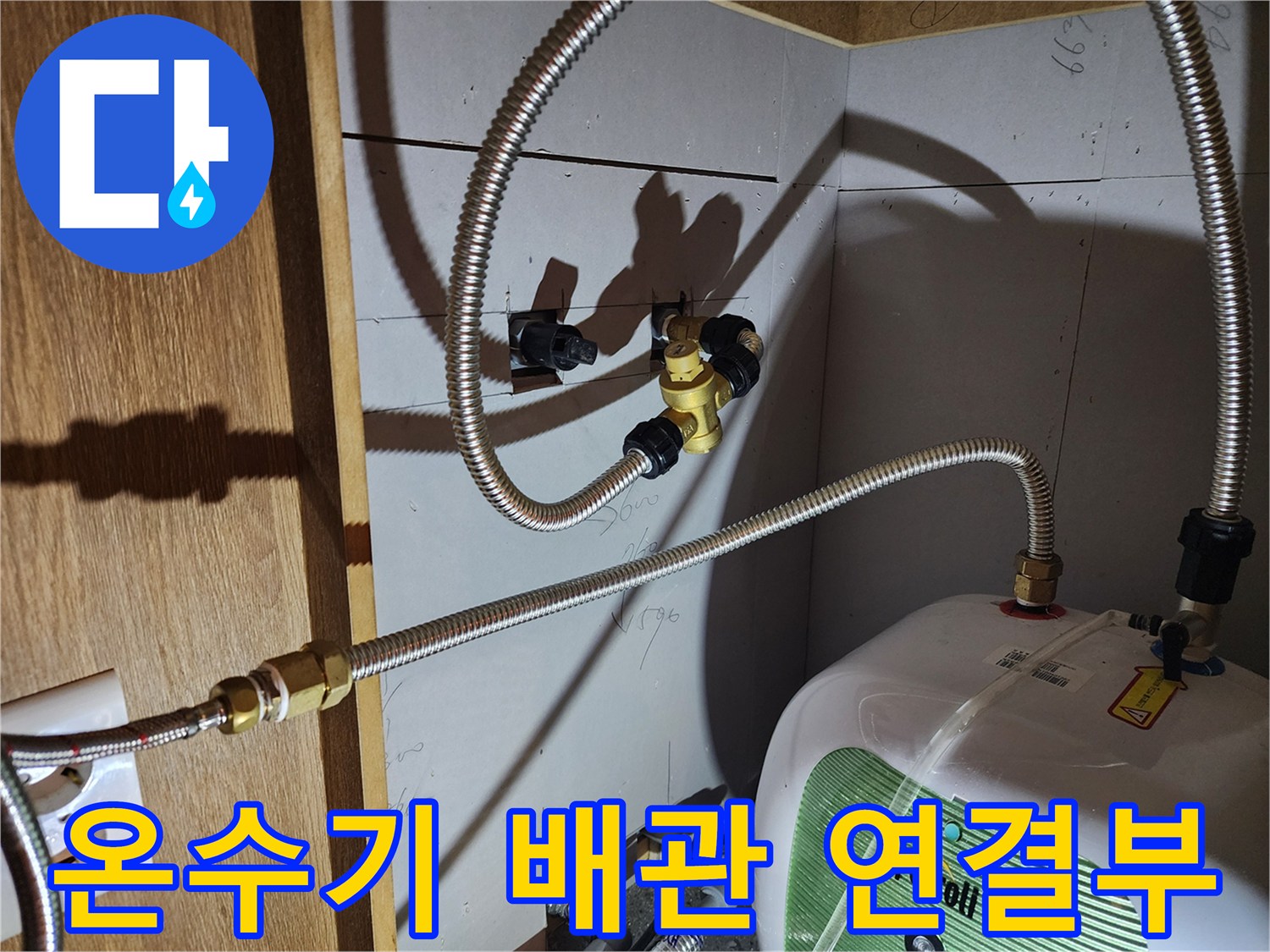 주방 하부장 내 설치된 전기 온수기와 금속 호스 연결 부위 상세 사진