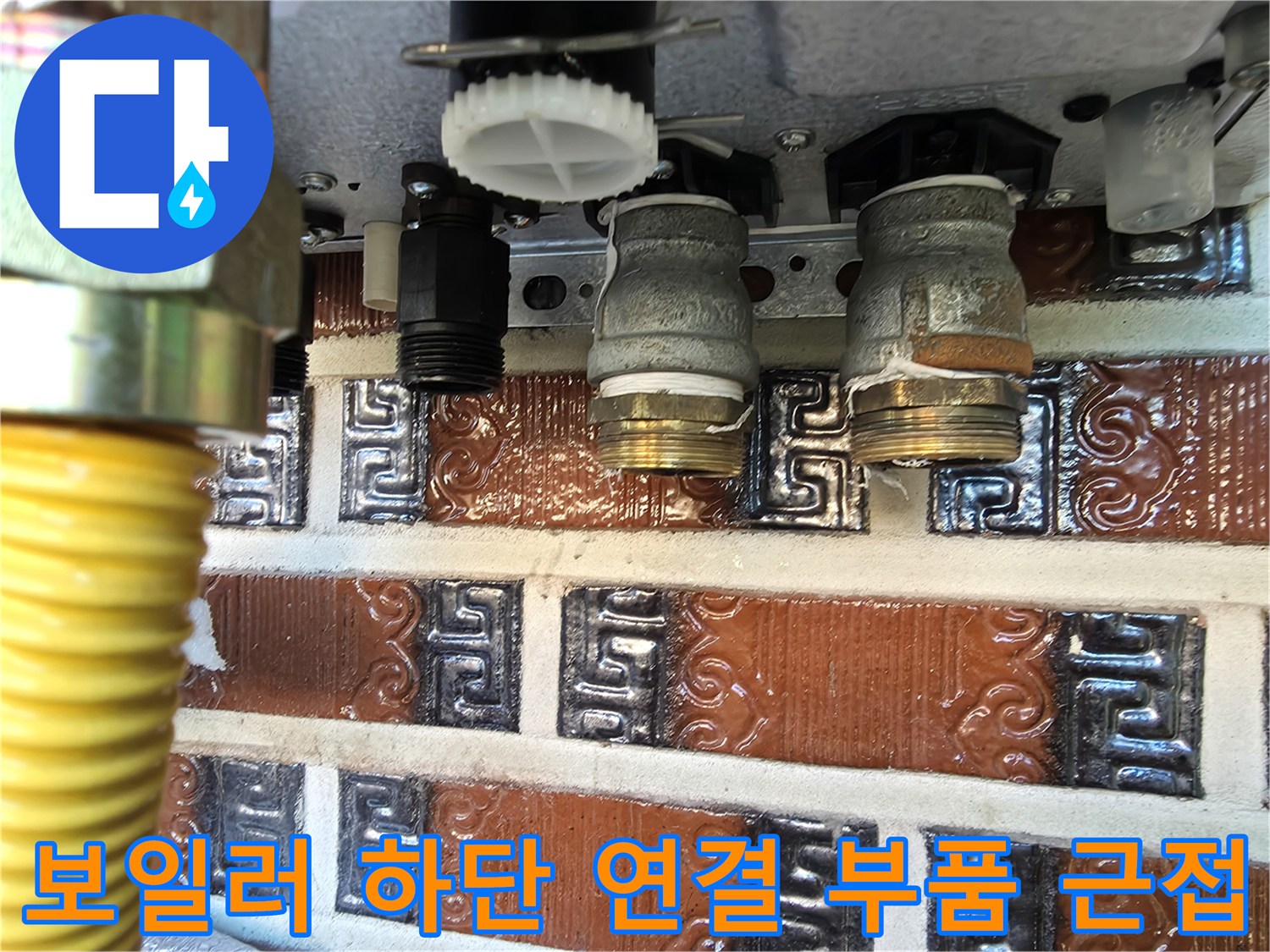 보일러 아래쪽 금속 재질의 배관 연결부와 노란색 호스 일부