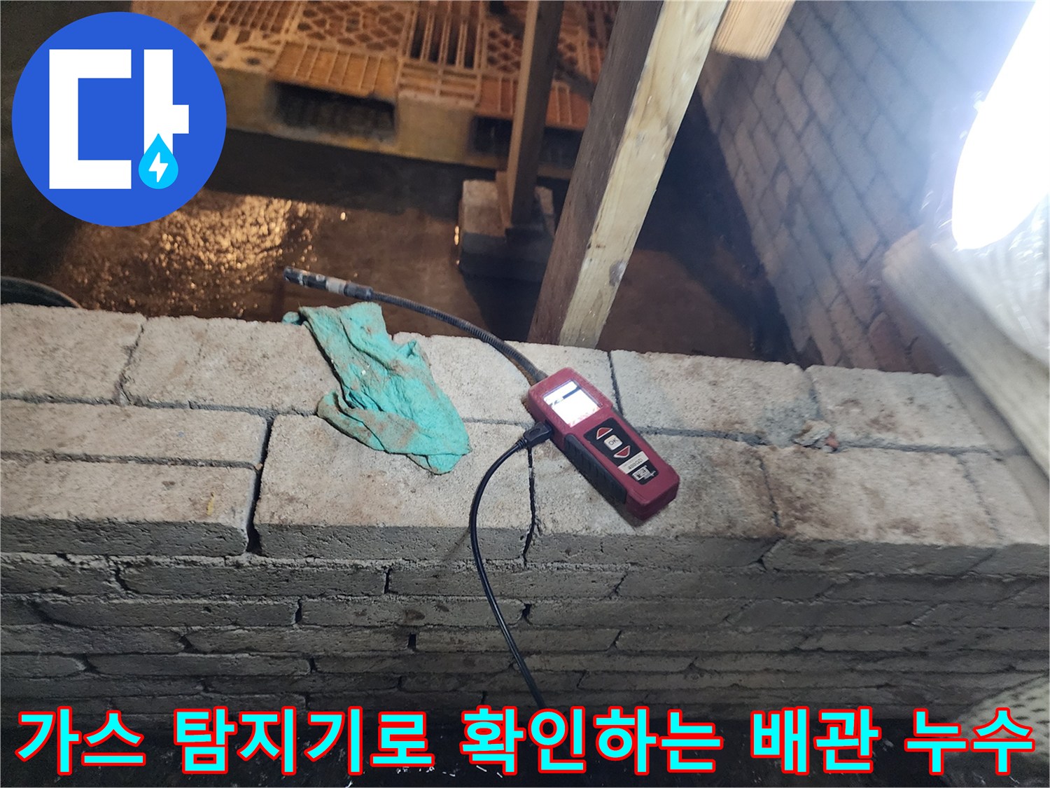 벽면 하단 벽돌 부근에서 가스 탐지기를 사용하여 매립된 배동 관의 미세한 누수 지점을 찾는 과정입니다.