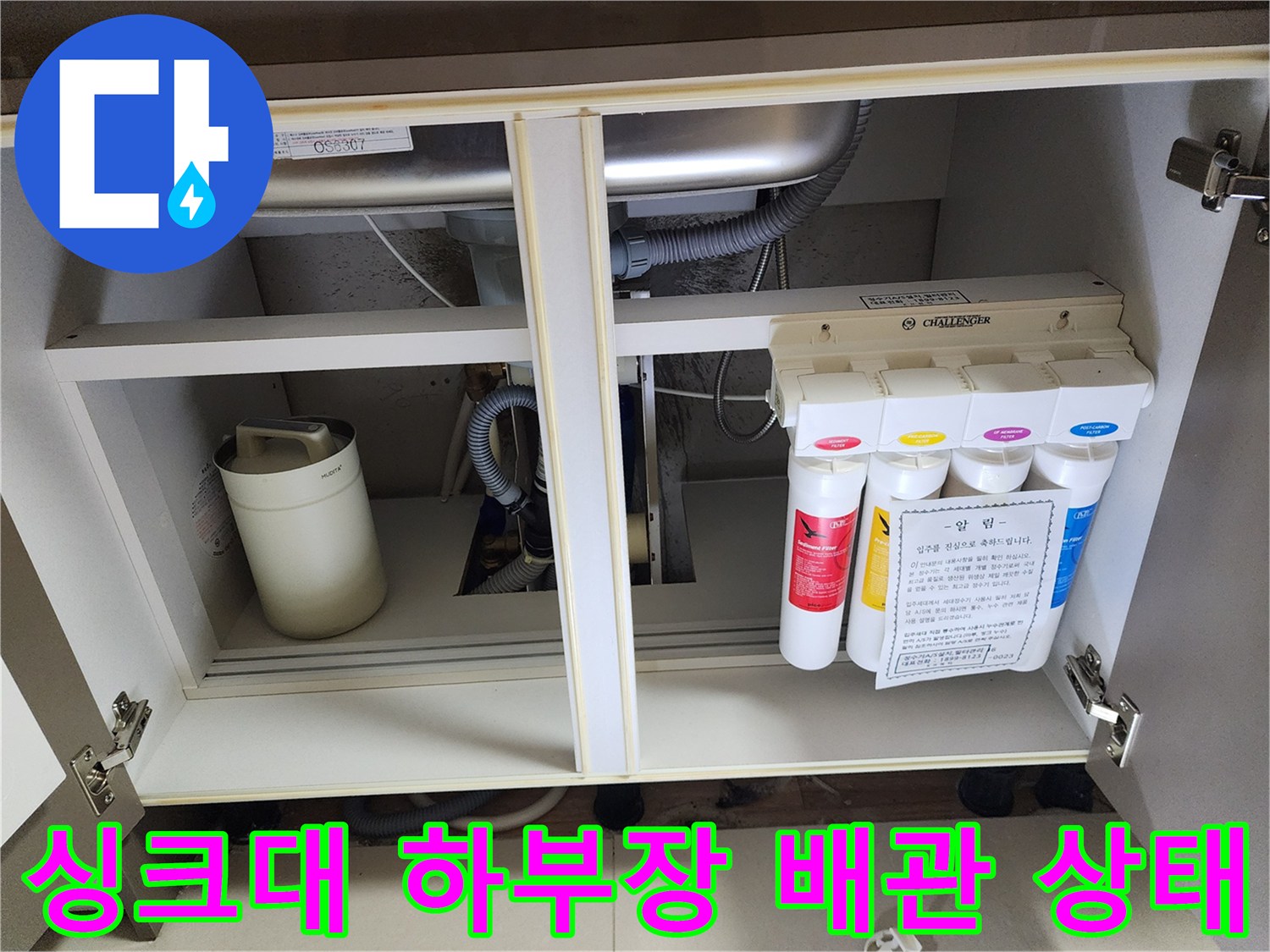 주방 싱크대 하부장 내부의 정수 필터와 배수 호스 연결 부위 모습