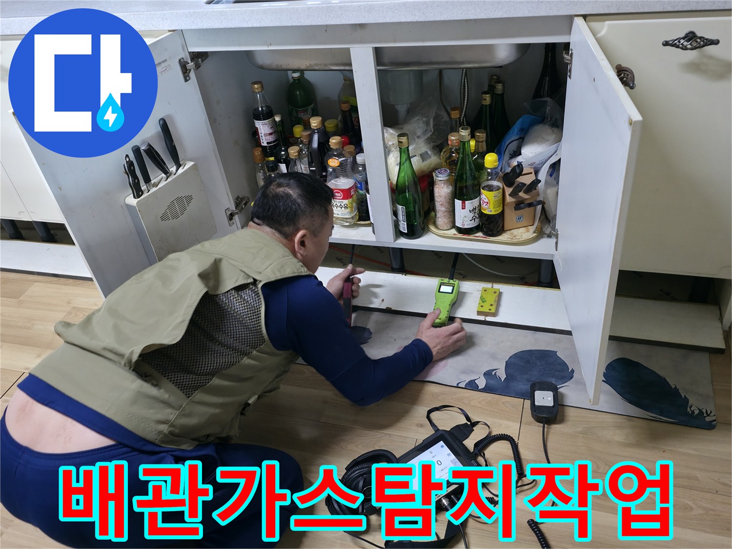 싱크대 하부 공간에서 가스 탐지기로 배관의 누수 반응을 추적하는 장면입니다.