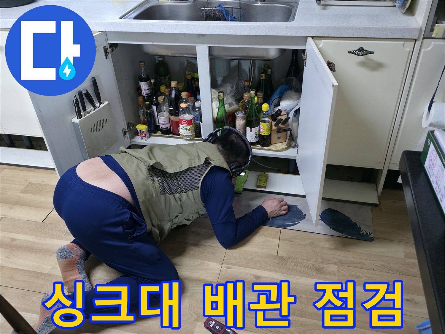 좁은 싱크대 하부 공간에서 배관 누수를 확인하는 엔지니어의 모습