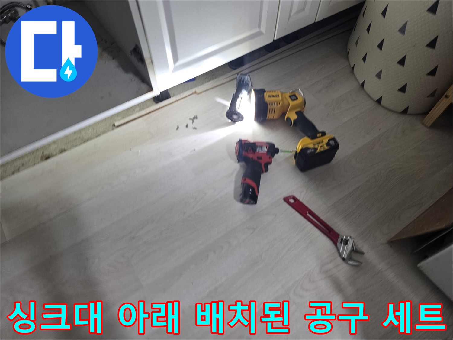 싱크대 하부 배관 점검을 위해 놓인 렌치와 전동 드릴