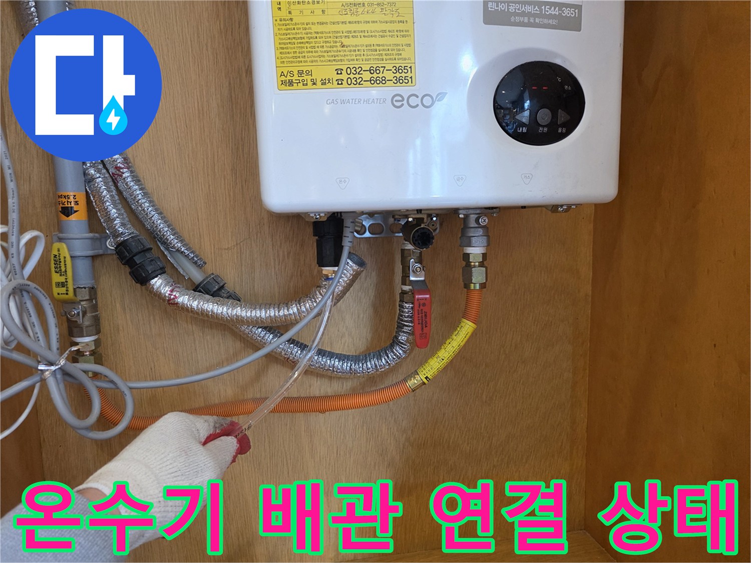 가스 온수기 하단에 연결된 은색 자바라 배관과 주황색 호스의 연결 부위 모습