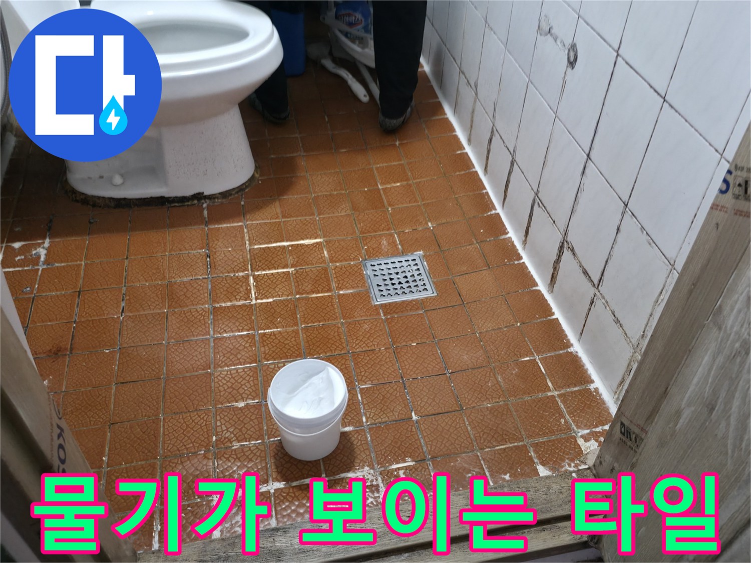 변기 주변의-젖은 타일 바닥과 배수구 모습입니다.