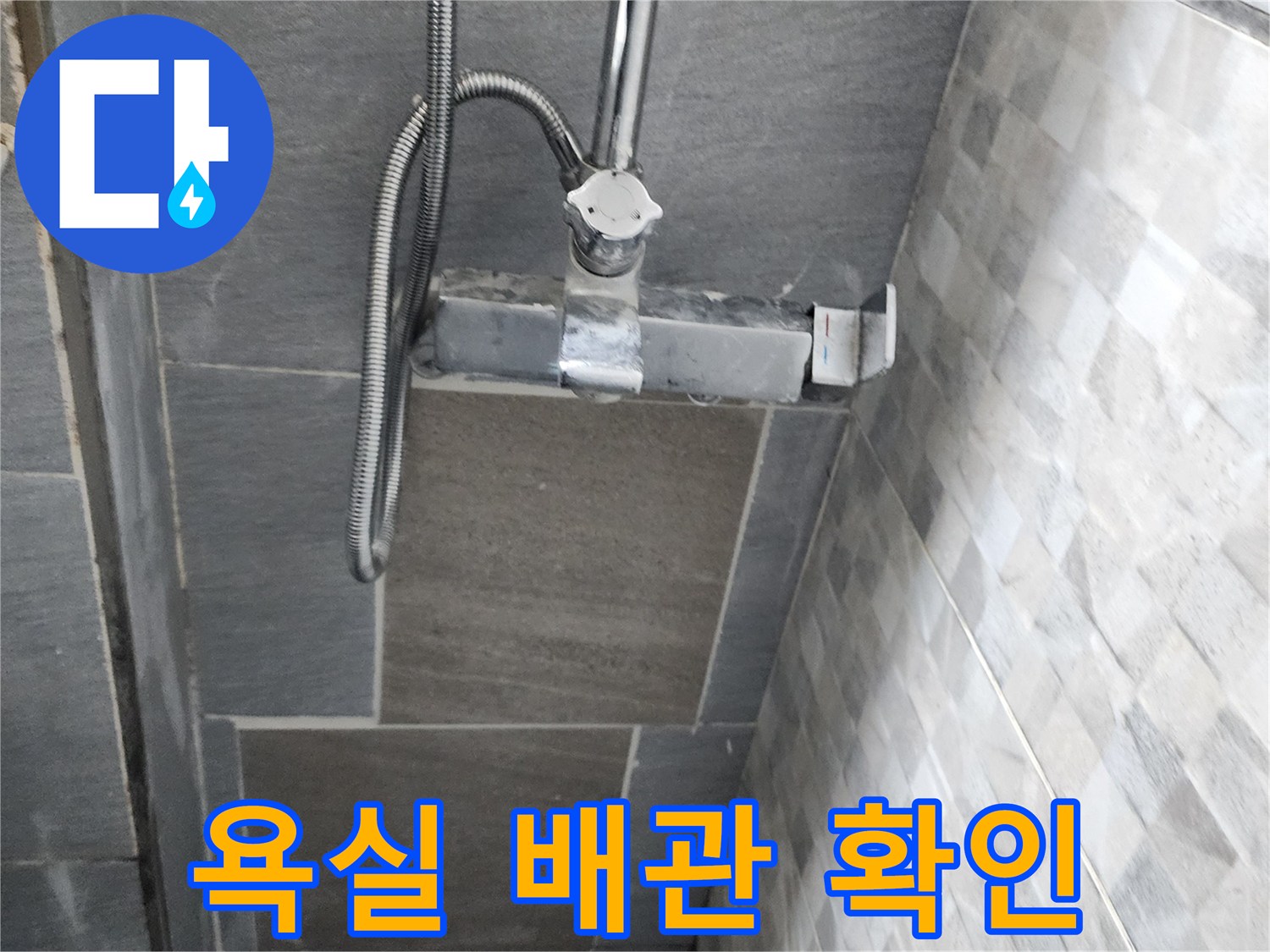 회색 타일 벽면에 설치된 수전 연결 부위 모습