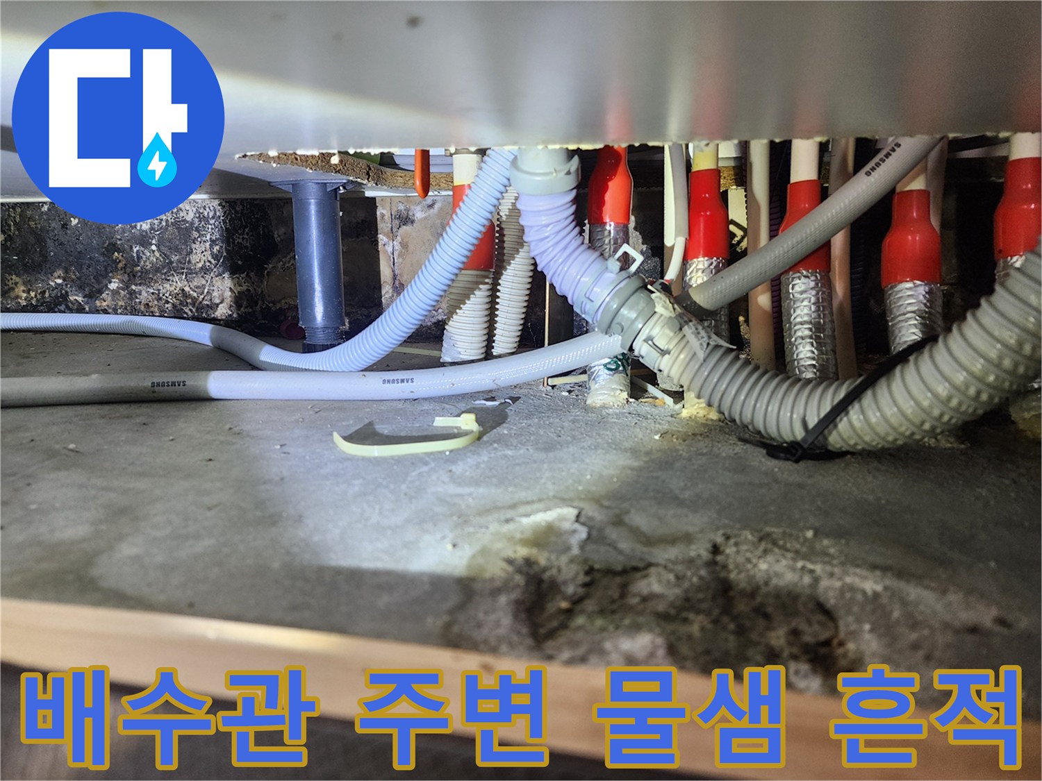 세탁기 배수구 근처의 젖은 바닥과 오염된 배관 연결부 촬영본