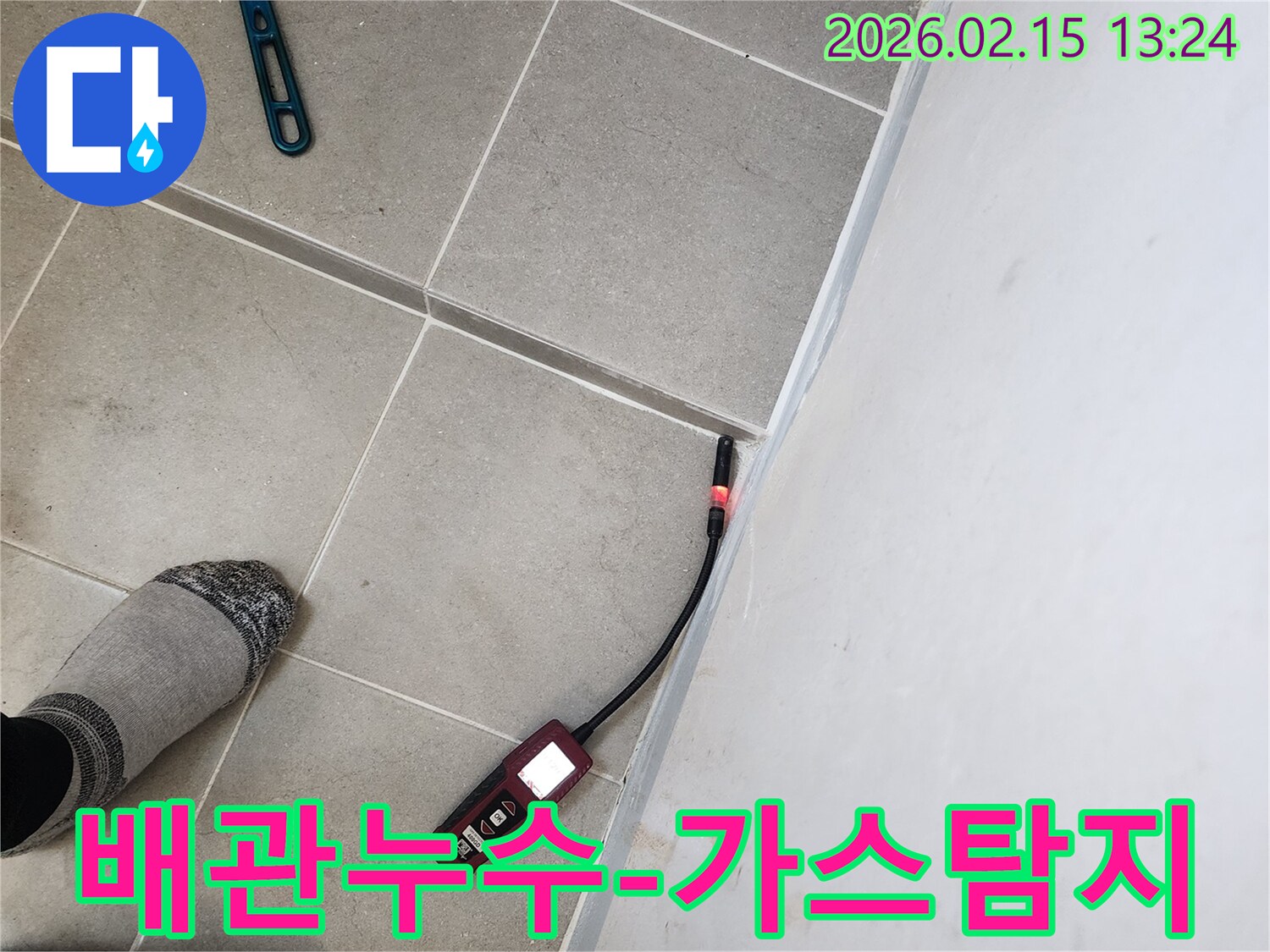누수 엔지니어가 바닥 타일과 벽면 경계에서 가스 누수탐지기를 이용해 배관 누수 지점을 찾는 모습