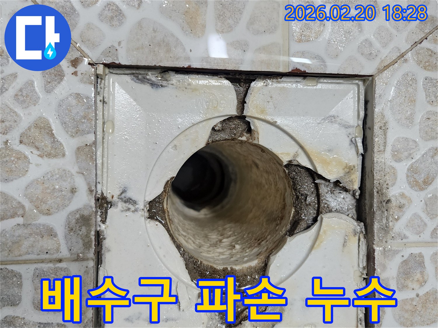 이 이미지는-오래된 욕실 배수구가 파손되어-주변 방수층이 손상되고-물이 새는 현장을-보여주고 있습니다