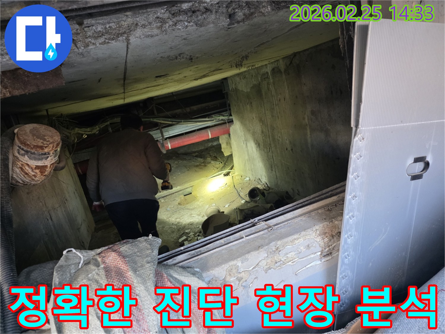 누수 전문 엔지니어가-어둡고 좁은 현장에서-손전등을 비춰가며-누수의 정확한 원인을-진단하기 위해-배관을 면밀히 분석하는 모습입니다.
