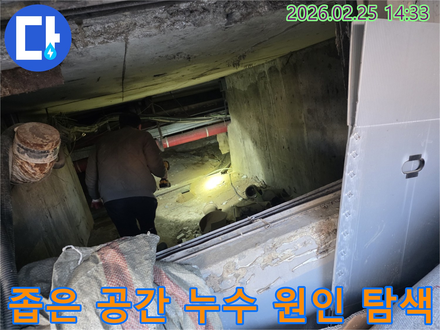 어둡고 협소한 공간에서-전문 엔지니어가-강력한 손전등으로-배관의 미세한 누수 지점을-정확히 찾아내기 위해-집중적으로 탐사하는 모습입니다.
