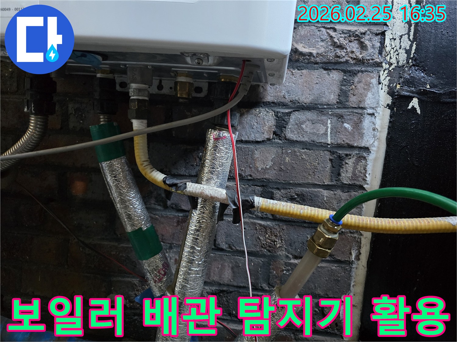 이 이미지는-벽에 설치된-보일러 하단부의-복잡한 배관 연결부와-전선-그리고-은색 단열재로-감싸진-파이프들을-보여주며-최신 누수 탐지기를-활용한-정밀한 점검이-진행되고-있음을-암시합니다.