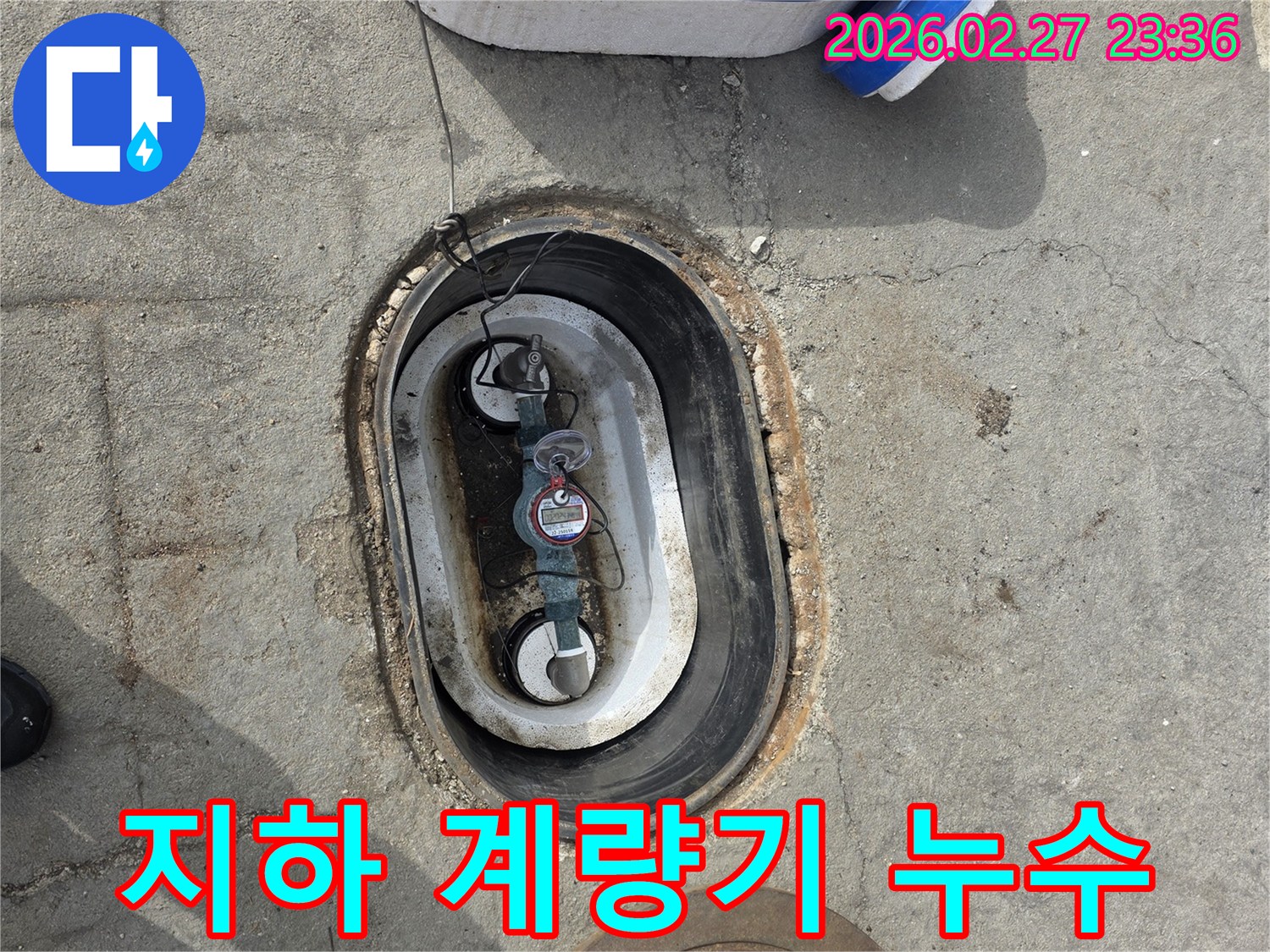 콘크리트 바닥에 설치된 수도 계량기에서-물이 새고 있는 현장을 보여주는 이미지입니다.