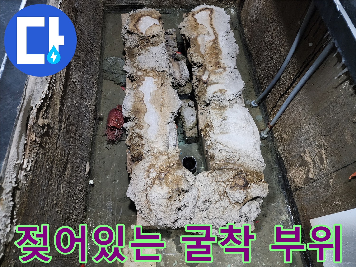 물에 젖은 배관과 단열재가 노출된 욕조 하부 모습입니다.