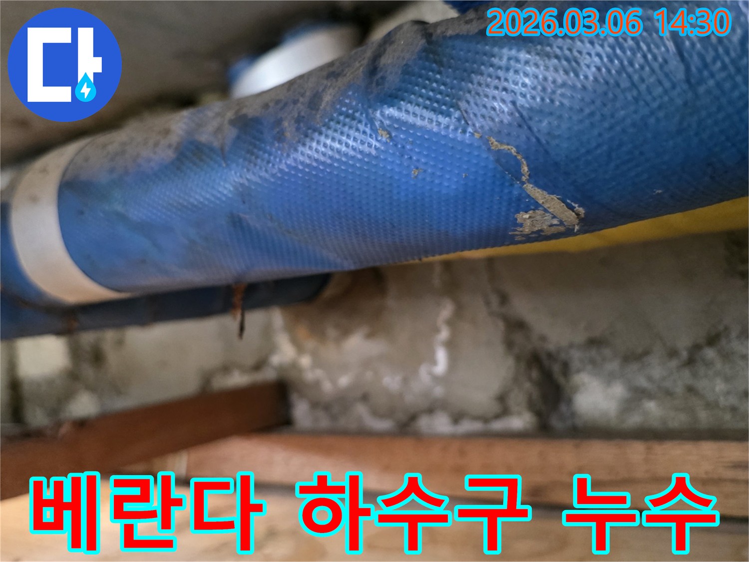 아파트 베란다 하부-파란색 배관과-젖은 콘크리트 벽면-그리고 나무 지지대를-정밀하게 점검하는 모습