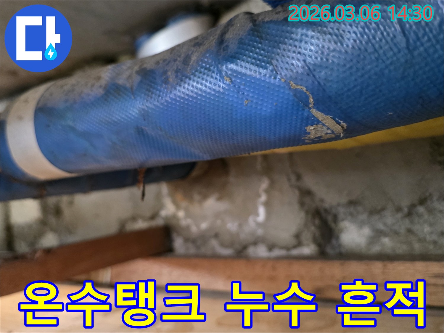 주택 온수탱크 하부-파란색 배관과-젖은 콘크리트 벽면-그리고 나무 지지대를-꼼꼼히 점검하는 모습