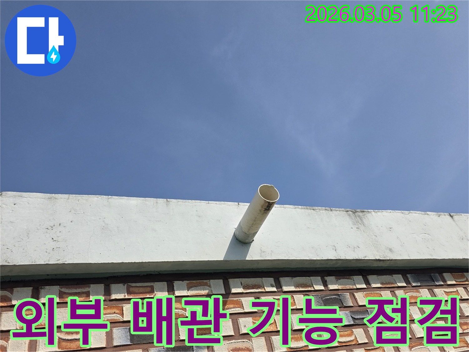 푸른-하늘과-벽돌-무늬-외벽을-배경으로-옥상에서-돌출된-배수관의-모습입니다.