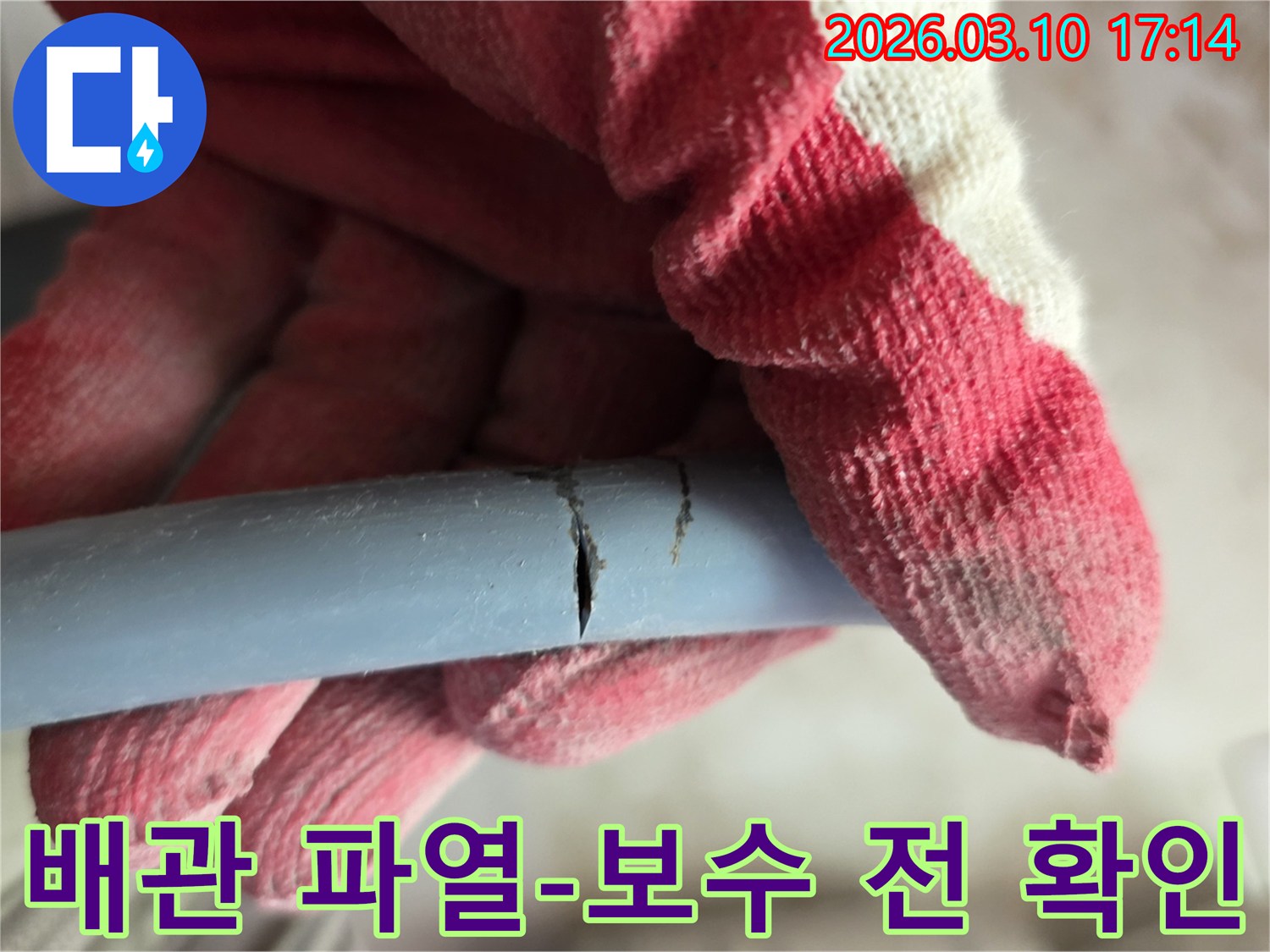 작업용 장갑을 착용한 손이-파열된 회색 배관을 잡고-누수 지점을 명확히 보여주고 있습니다