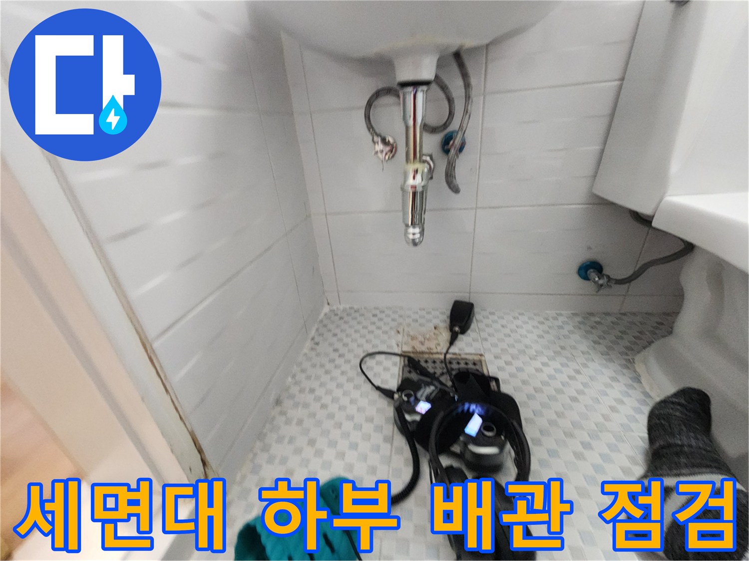 세면대 아래 배관에 연결된 디지털 압력계와 작업용 헤드셋 사진입니다.