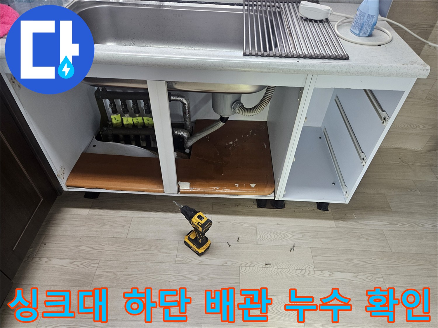 싱크대 아래 분배기 주변의 젖은 바닥과 배관 연결 부위