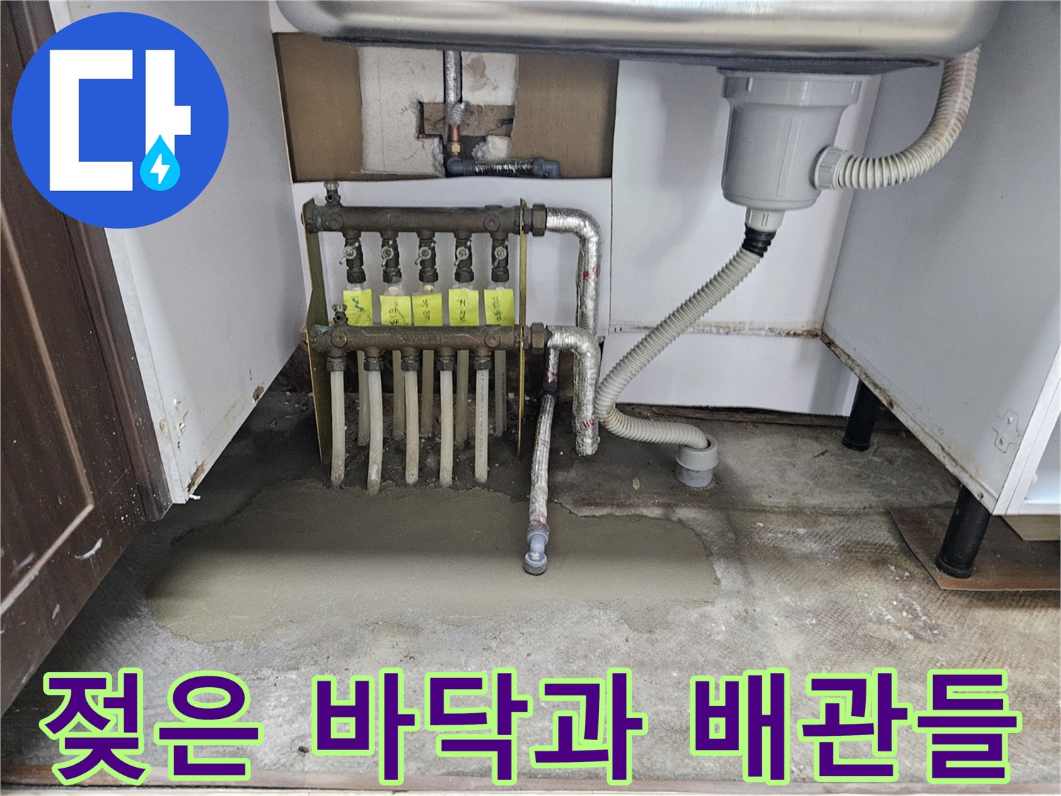 싱크대 하단 분배기 주변의 젖은 바닥면과 노출된 배관 부위