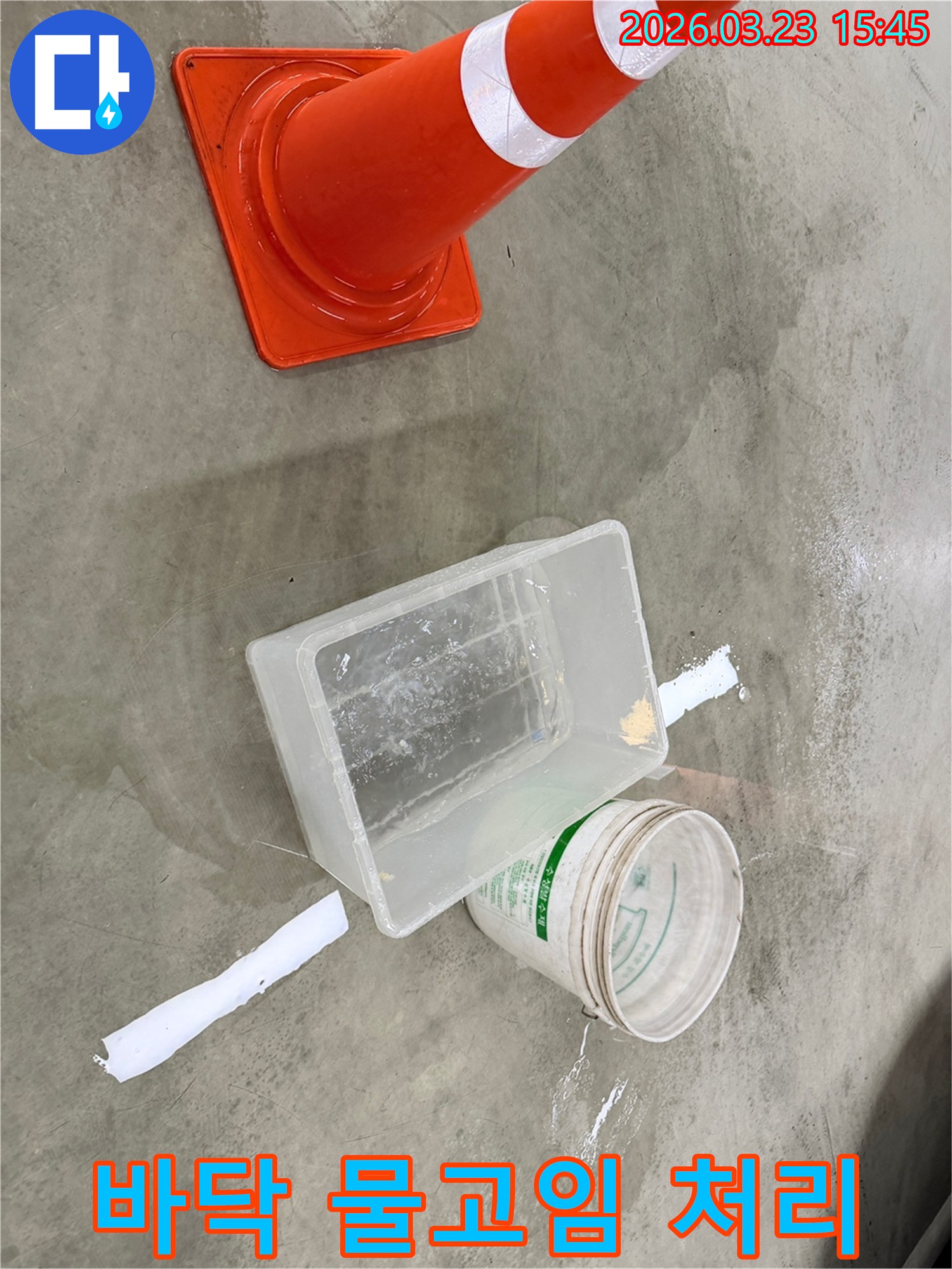 바닥에 물기가 흥건한 누수 현장에서-안전 콘과 물받이 용기를 사용하여 상황을 관리하고 있습니다.
