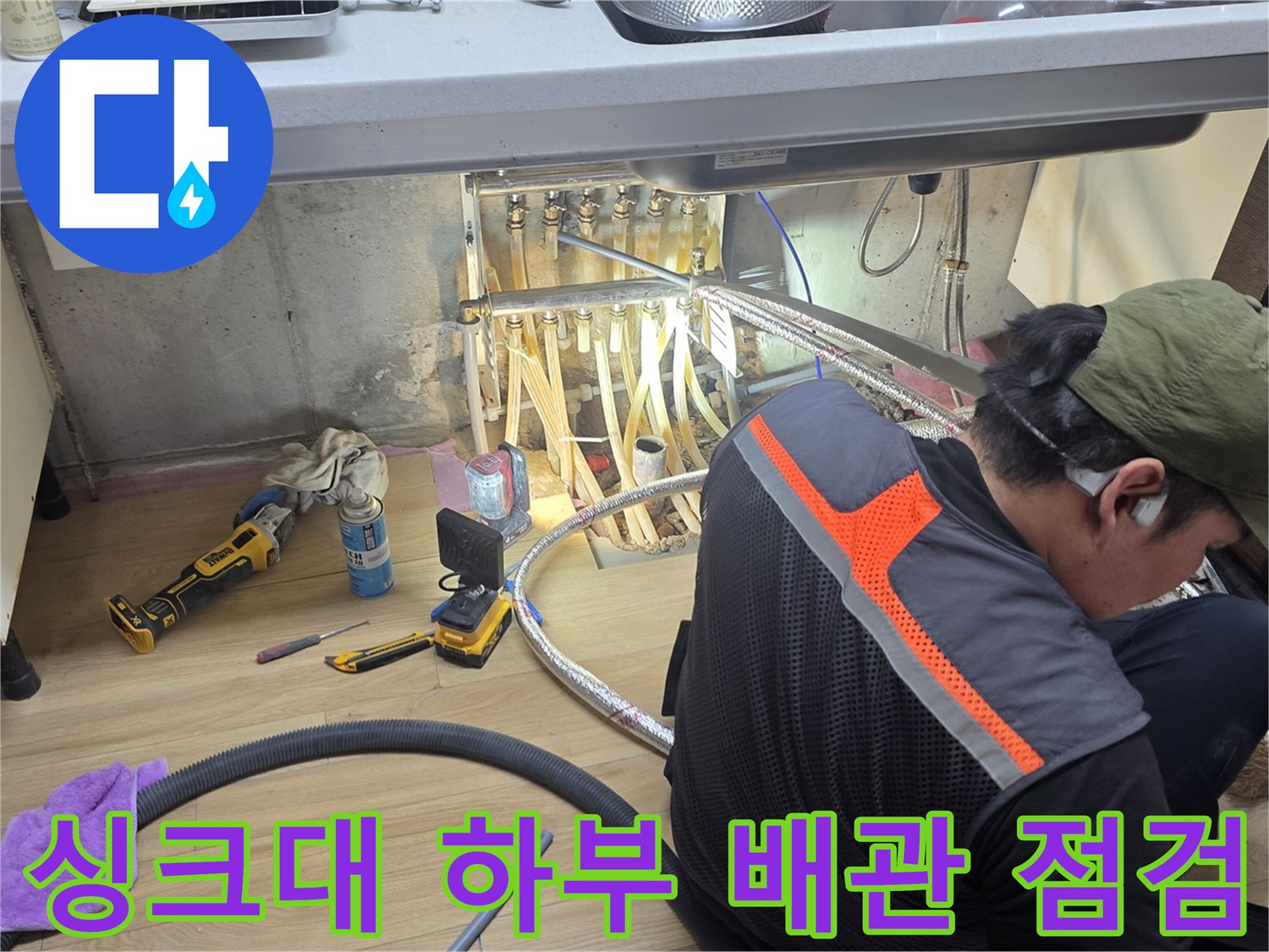 작업자가 싱크대 밑 공간의 배관을 세심하게 관찰하는 장면