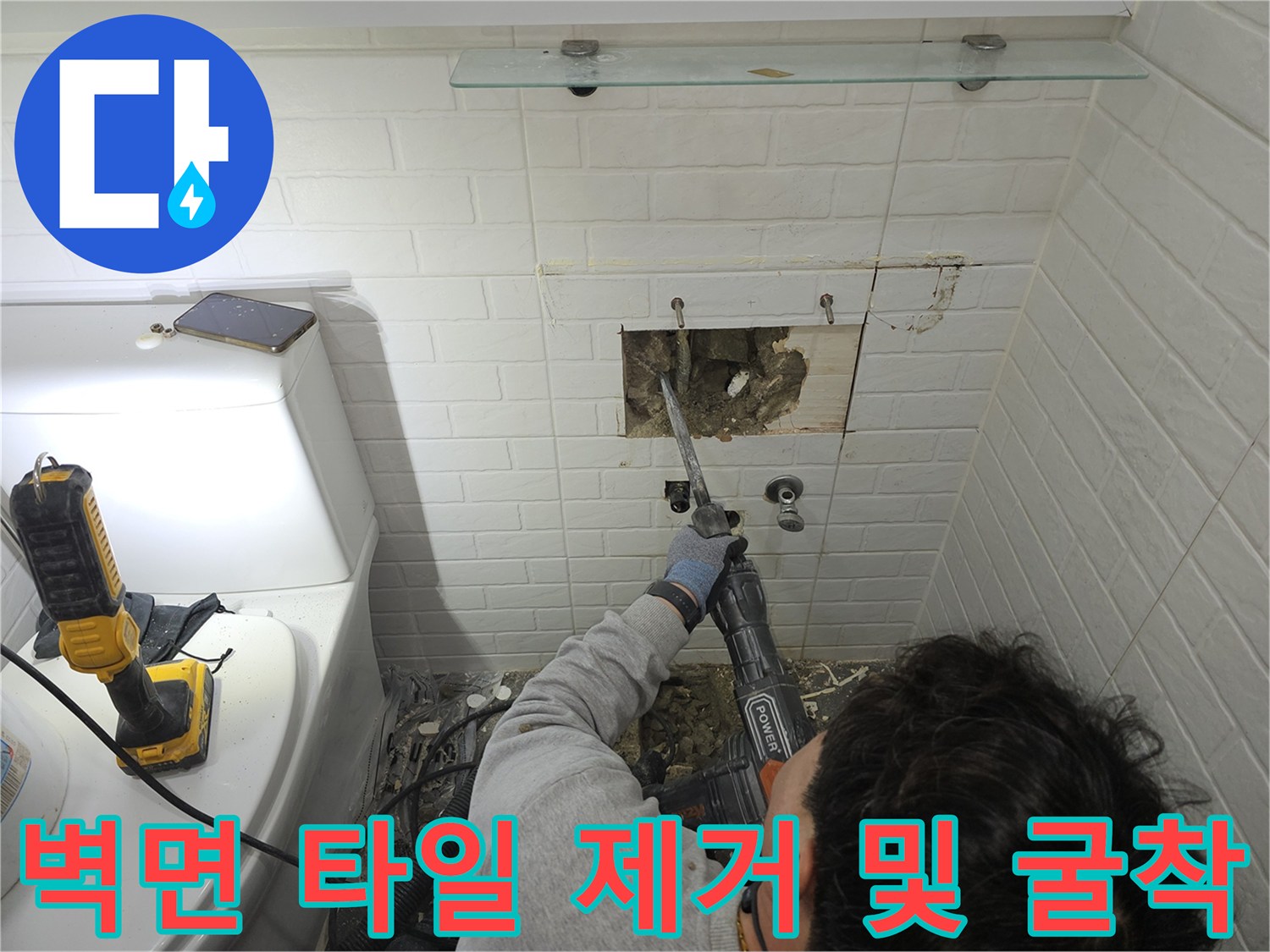 전동 장비를 사용하여 화장실 벽면의 콘크리트를 파쇄하여 배관을 노출시키는 모습