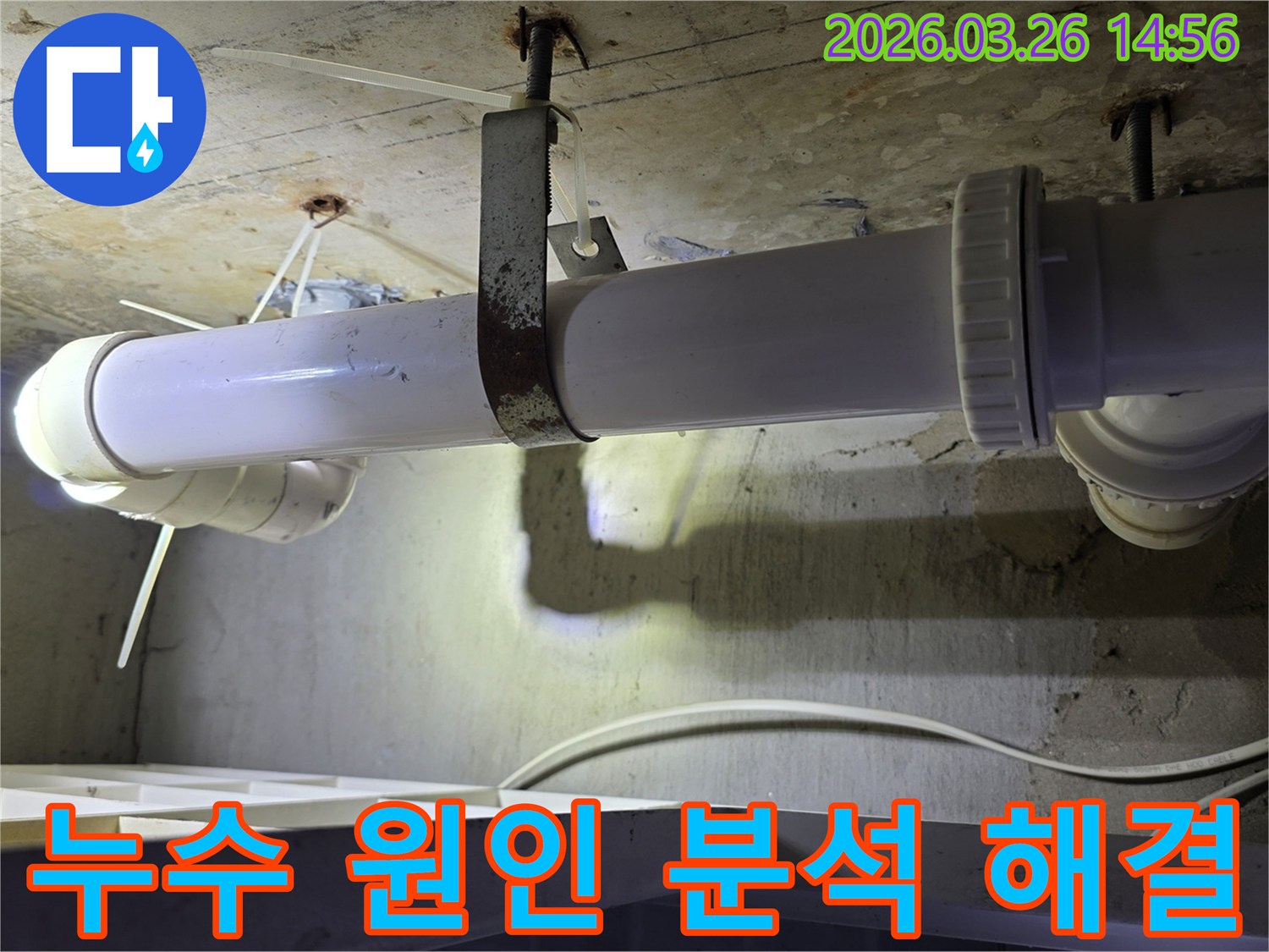 콘크리트 천장에 고정된-하얀색 배관의 연결 부위와-녹슨 지지대를 엔지니어가-면밀히 점검하는 모습으로-누수 원인 분석 과정을 보여줍니다