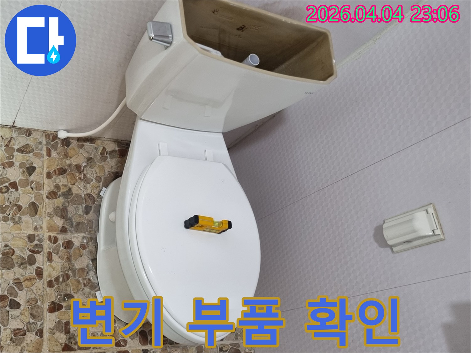 변기 물탱크가 열려 내부 부품이 노출된 상태로-수평계가 변기 시트 위에 놓여-부품 노후 여부를 확인하고 있습니다