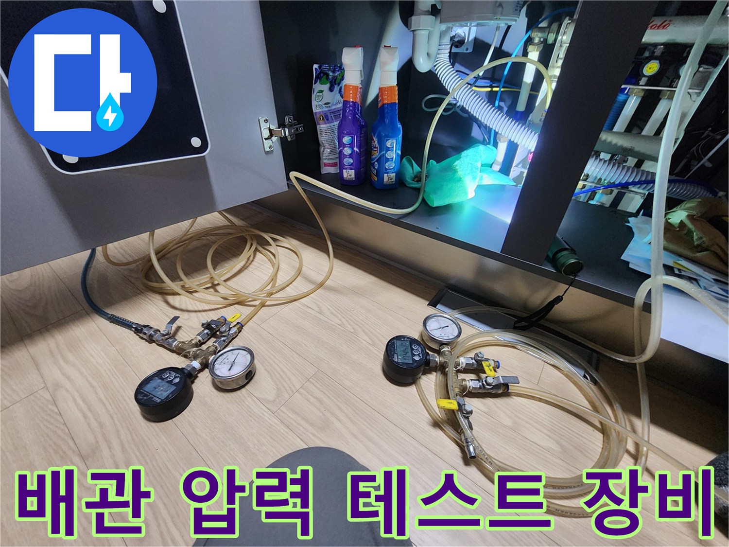 누수 지점을 찾기 위해 싱크대 밑에 배치된 압력 측정 기구와 가스 호스들