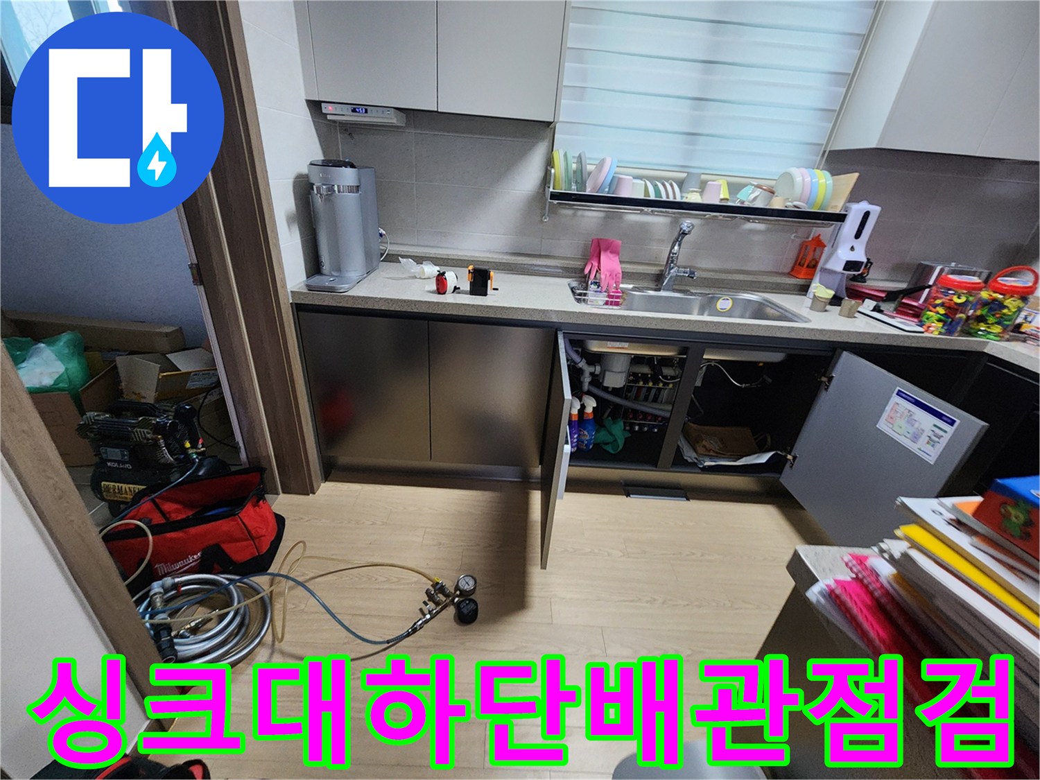 주방 싱크대 하부장 내부의 복잡한 배관과 가스 탐지 장비 모습