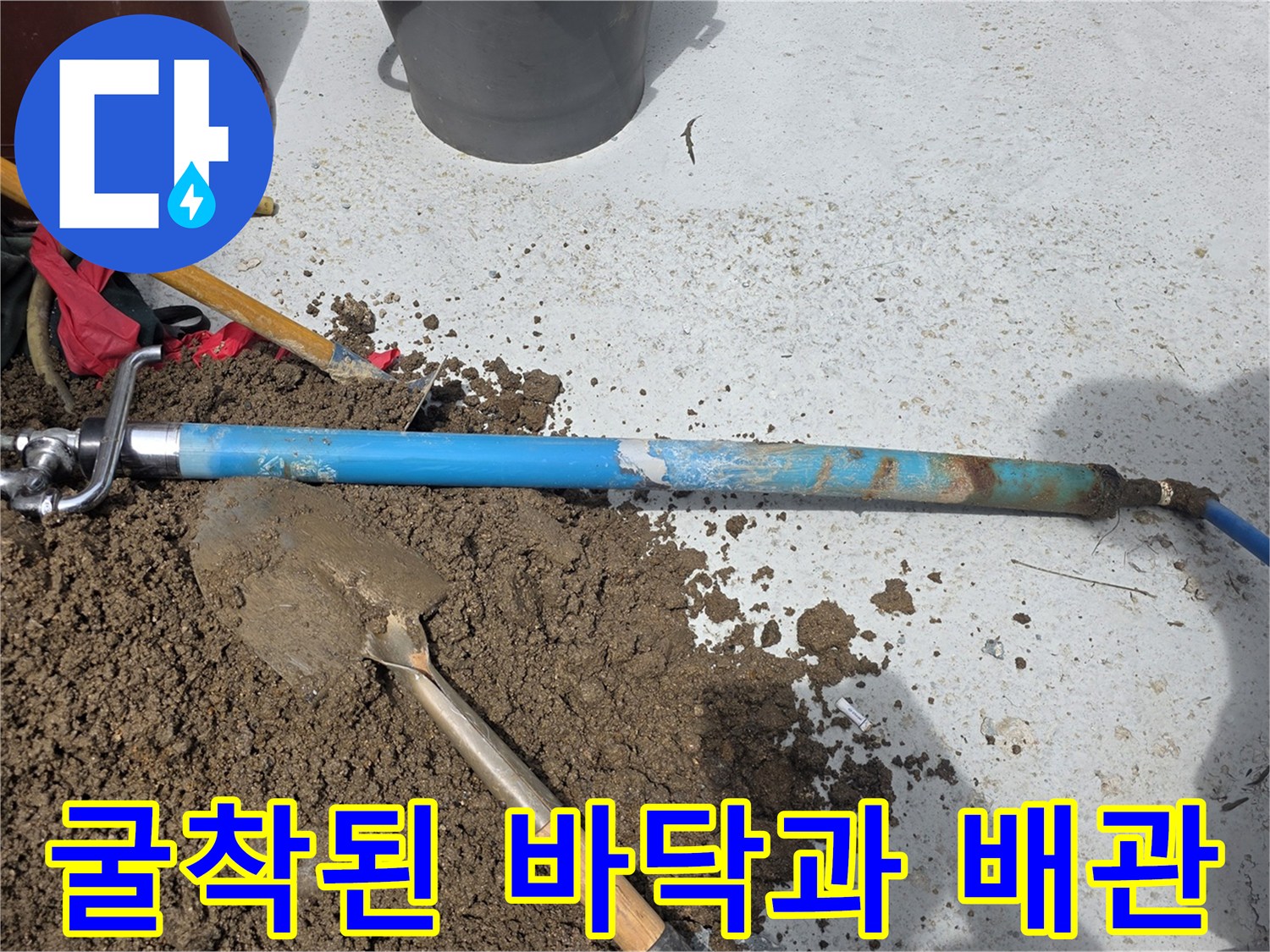 작업용 삽과 흙이 파헤쳐진 곳에 놓인 파란색 수도관