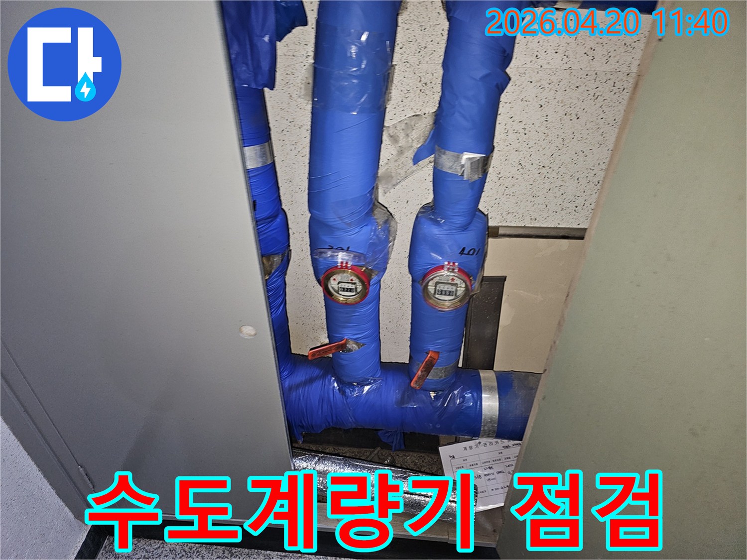 파란색 단열재로-감싸진-수도관과-두 개의-수도계량기가-보이는-누수-점검-현장-사진입니다.