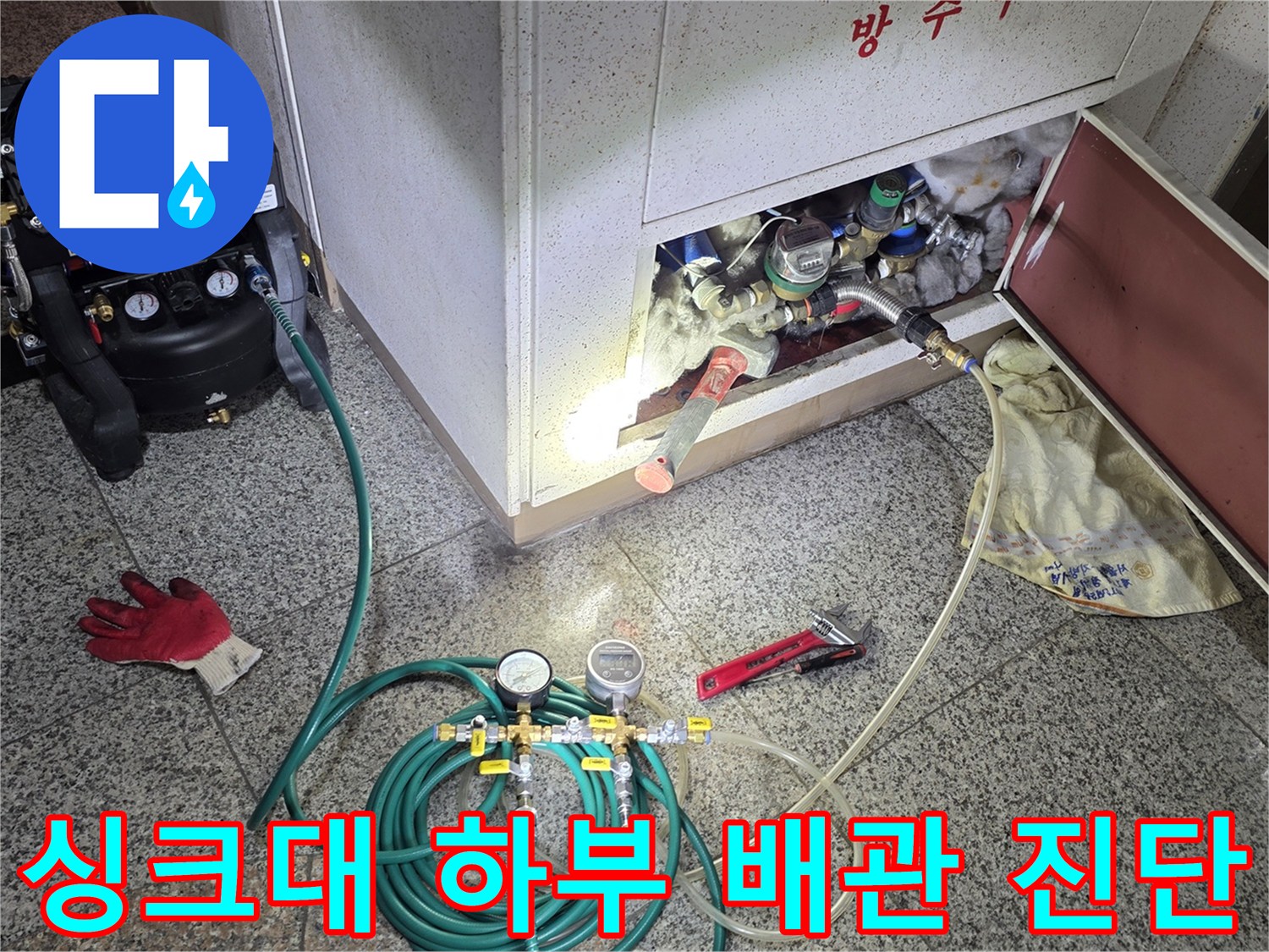 주방 싱크대 아래 분배기 함에 압력 측정용 게이지와 호스를 연결한 현장 사진입니다.