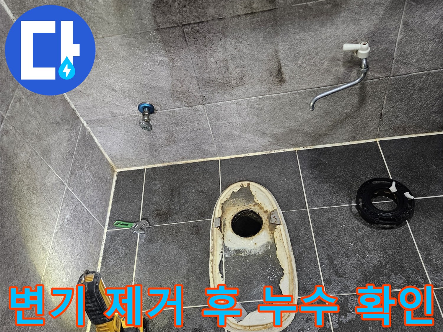 변기가 제거된 욕실 바닥의 배수구와-주변 타일에 나타난 물에 젖은 흔적을-손전등으로 밝혀 누수 지점을 확인하는 과정입니다.