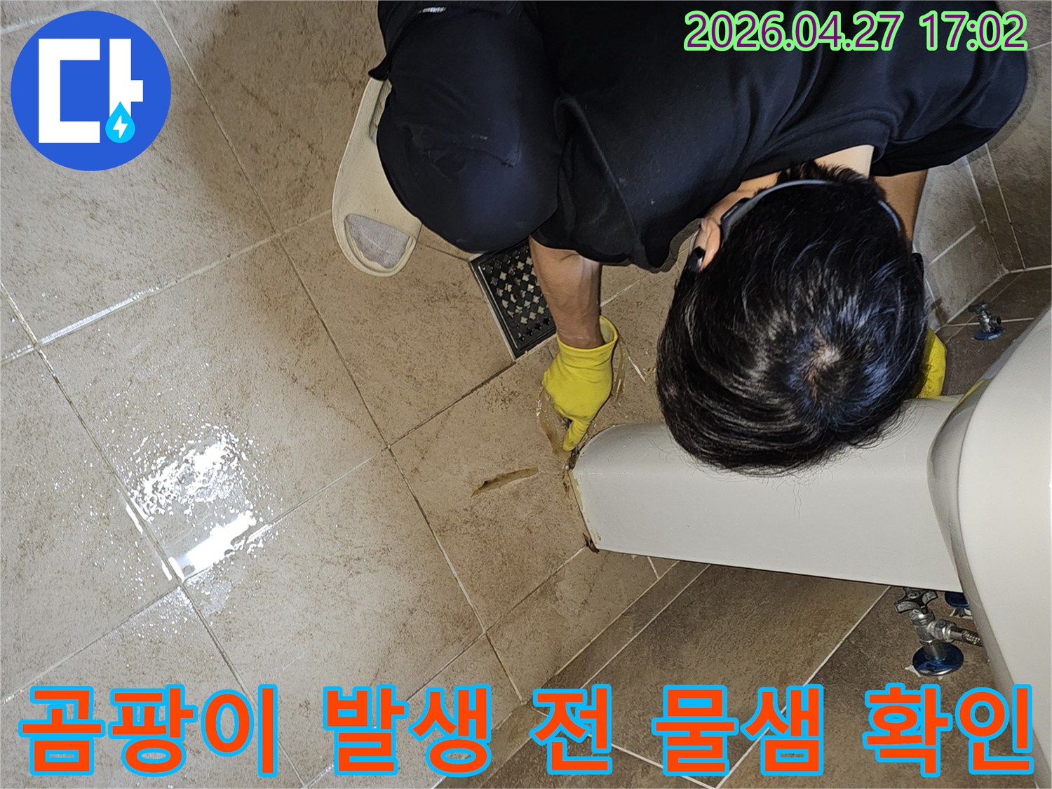전문 엔지니어가-노란 장갑을 끼고-욕실 바닥의 젖은 타일과-세면대 하단부를-집중적으로 관찰하며-곰팡이 발생 전 물샘을 확인합니다