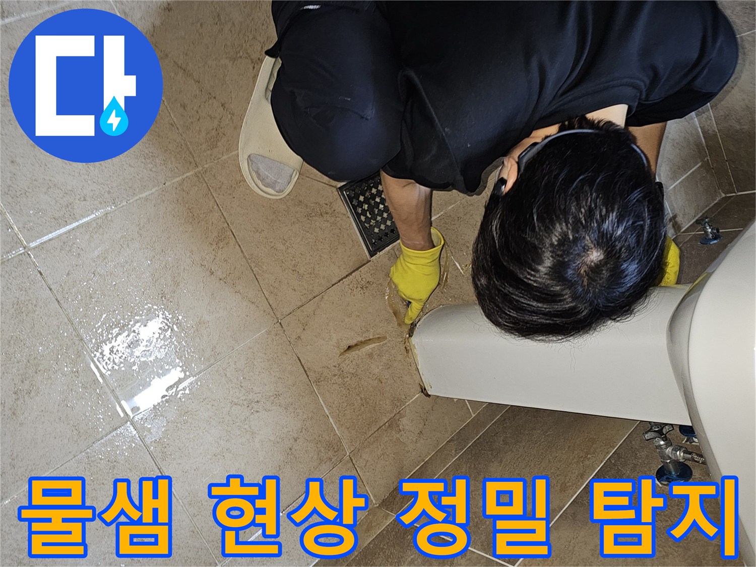 전문 엔지니어가-노란 장갑을 끼고-욕실 바닥의 젖은 타일과-세면대 하단부를-집중적으로 관찰하며-누수 지점을 정밀하게 탐지하고 있습니다
