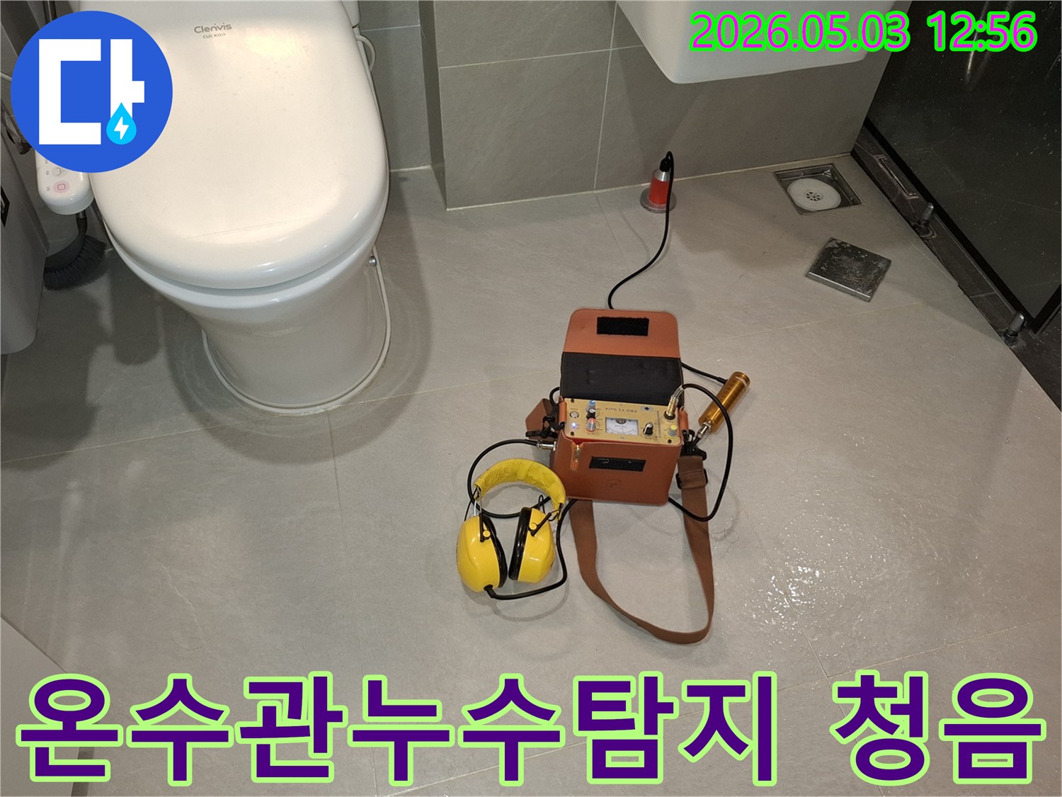 욕실 바닥에 설치된-누수 탐지 장비와-헤드폰을 사용하여-온수관 누수음을 듣고 있는 모습